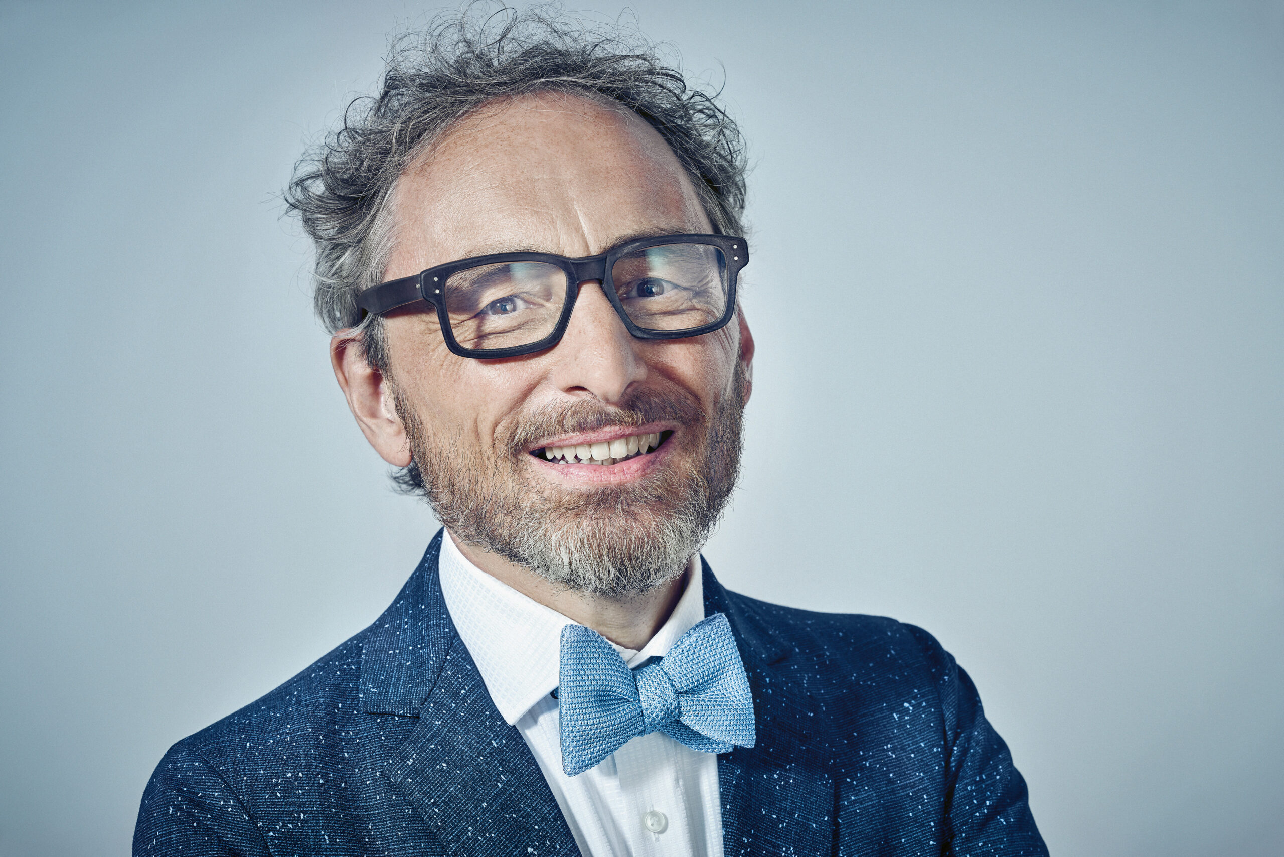 Christoph Holz über KI, Netzwerken und echte Verbindungen bis 2040 Porträt von Christoph Holz mit Brille und blauer Fliege vor hellem Hintergrund.